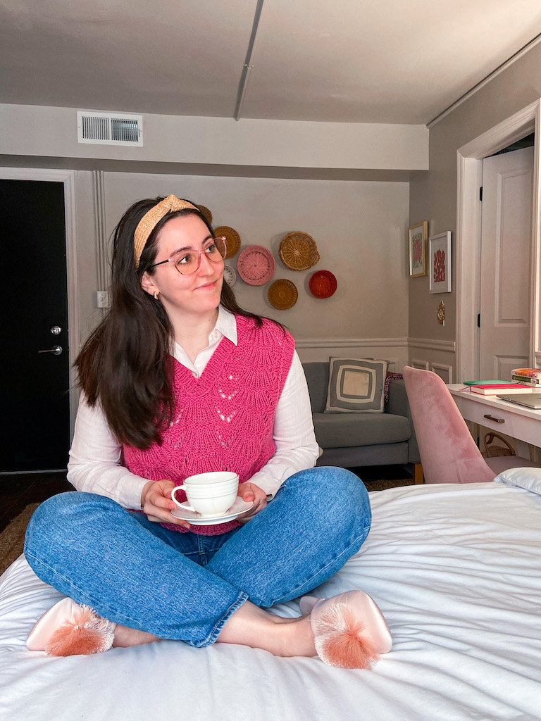 Styling a Pink Sweater Vest for Valentine's Day. Image description: pink button down under a pink knit sweater vest, blue jeans, and pink pom slippers.