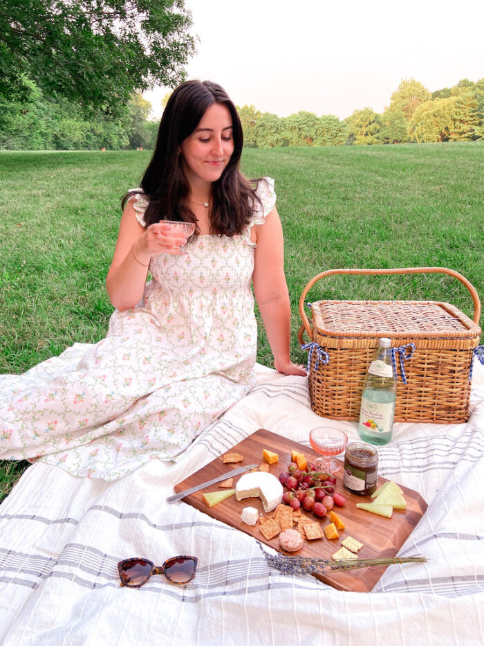 Image description: Kyndal sitting on a picnic blanket next to a picnic basket and snacks.
