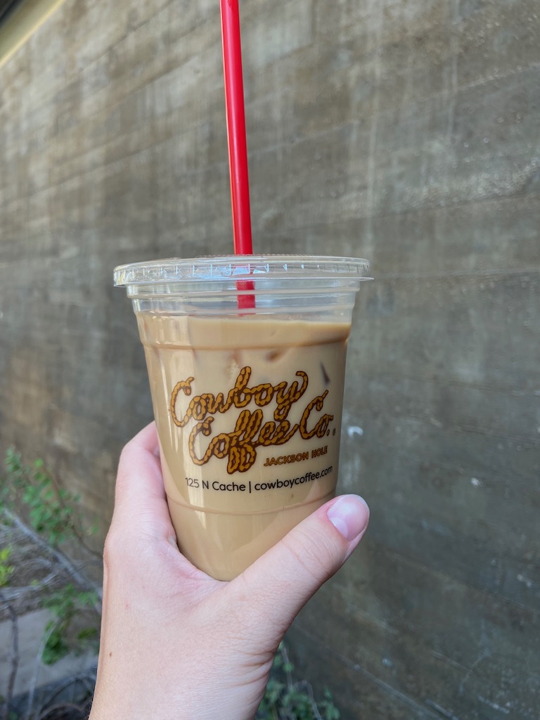 Image description: a white woman's hand holding up an iced latte from Cowboy Coffee co. in Jackson, Wyoming.