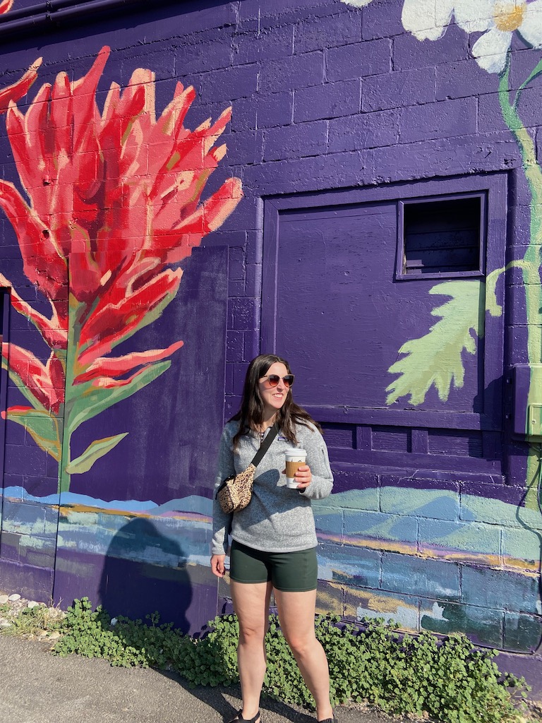 Grand Teton National Park & Jackson Hole Travel diary. Image description:  a white woman standing in front of a floral mural with a purple background.