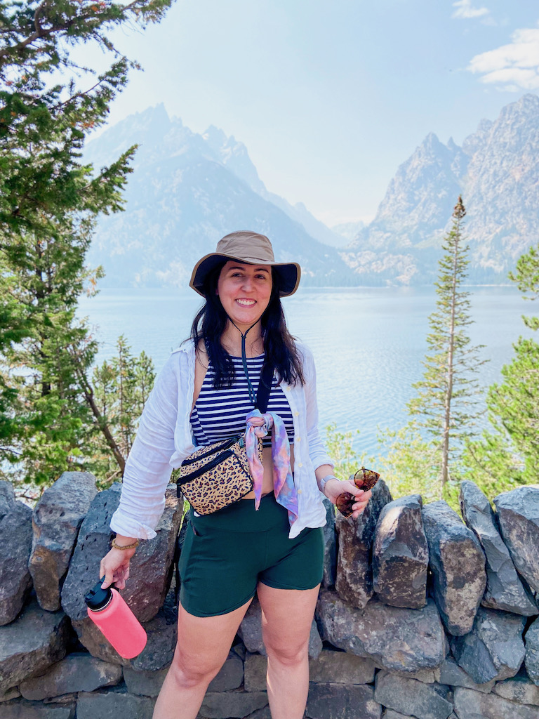 Image description: a white woman standing in front of the Grand Tetons and Jenny Lake.