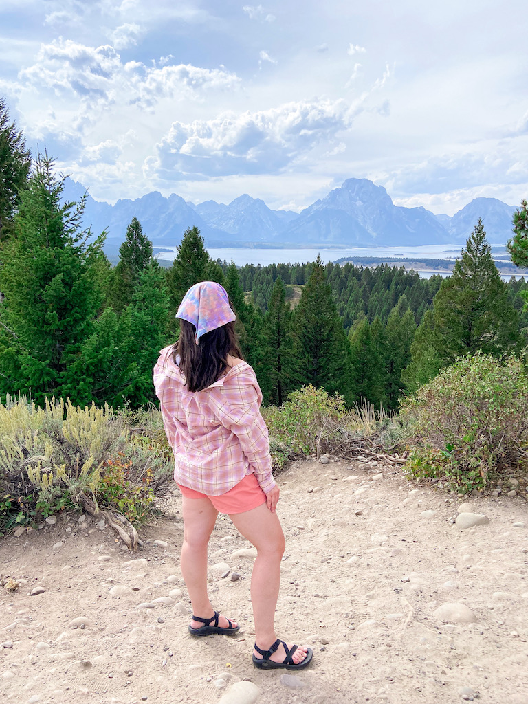 Grand Teton National Park and Jackson Hole travel diary. Image description: a white woman standing at a scenic overlook facing the Grand Tetons 
