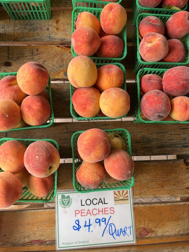 Image description: several baskets of local peaches for sale at a market.