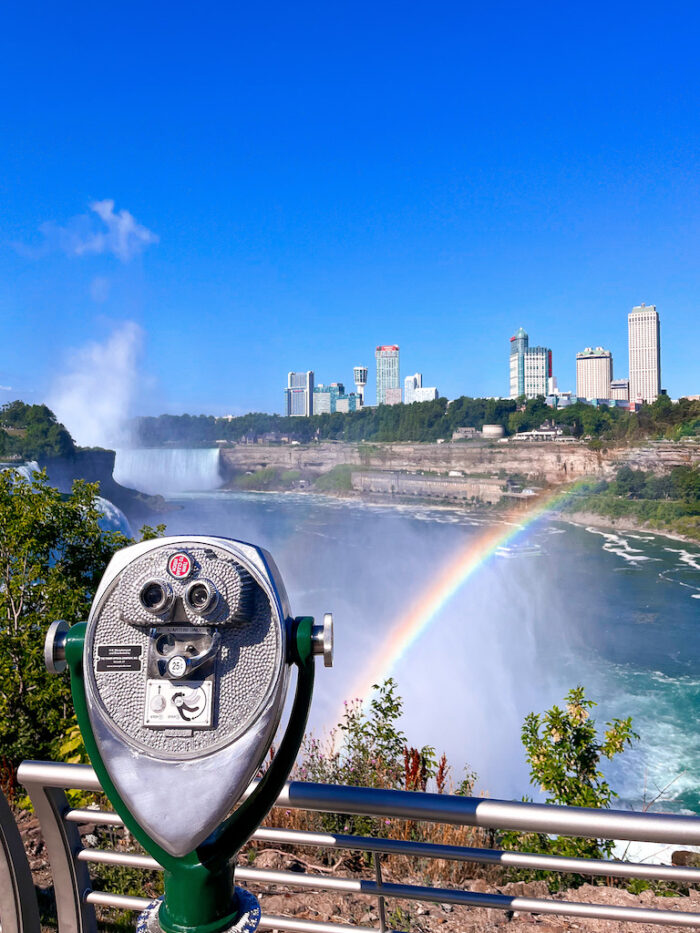 Image description: a tower viewer sits in front of Niagara Falls. A rainbow is just in front of the water.
